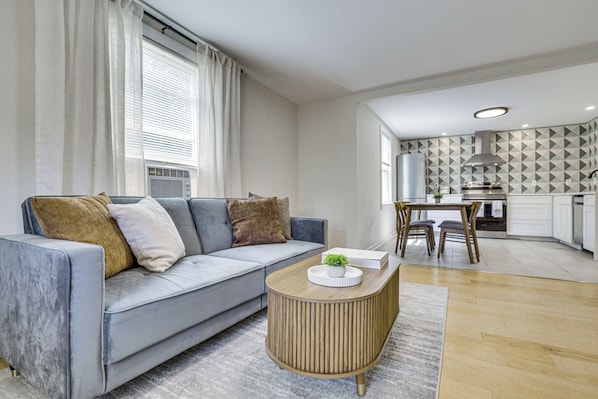 A modern living room with a grey sofa, a wooden coffee table, and a kitchen in the background. - 1 Mi to Caverns! Shenandoah Valley Apartment (Luray)