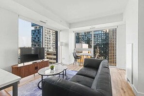 A modern living room with a flat-screen TV, a sofa, a coffee table, and a dining area with chairs. - 2 Bedroom/2 Bathroom Suite (Montreal)