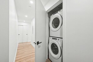 A laundry room with two front-loading washing machines, a wooden floor, and a white door. - 2 Bedroom/2 Bathroom Suite (Montreal)