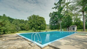 Ein rechteckiger Pool mit einer Leiter, umgeben von einer Steinterrasse und einer Rasenfläche mit Bäumen.