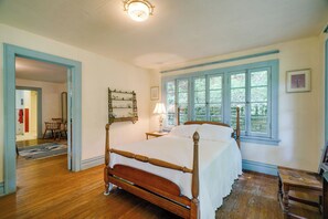 Ein traditionell eingerichtetes Schlafzimmer mit einem hölzernen Bett, einem Nachttisch, einer Lampe und einem Fenster mit Blick auf Bäume.