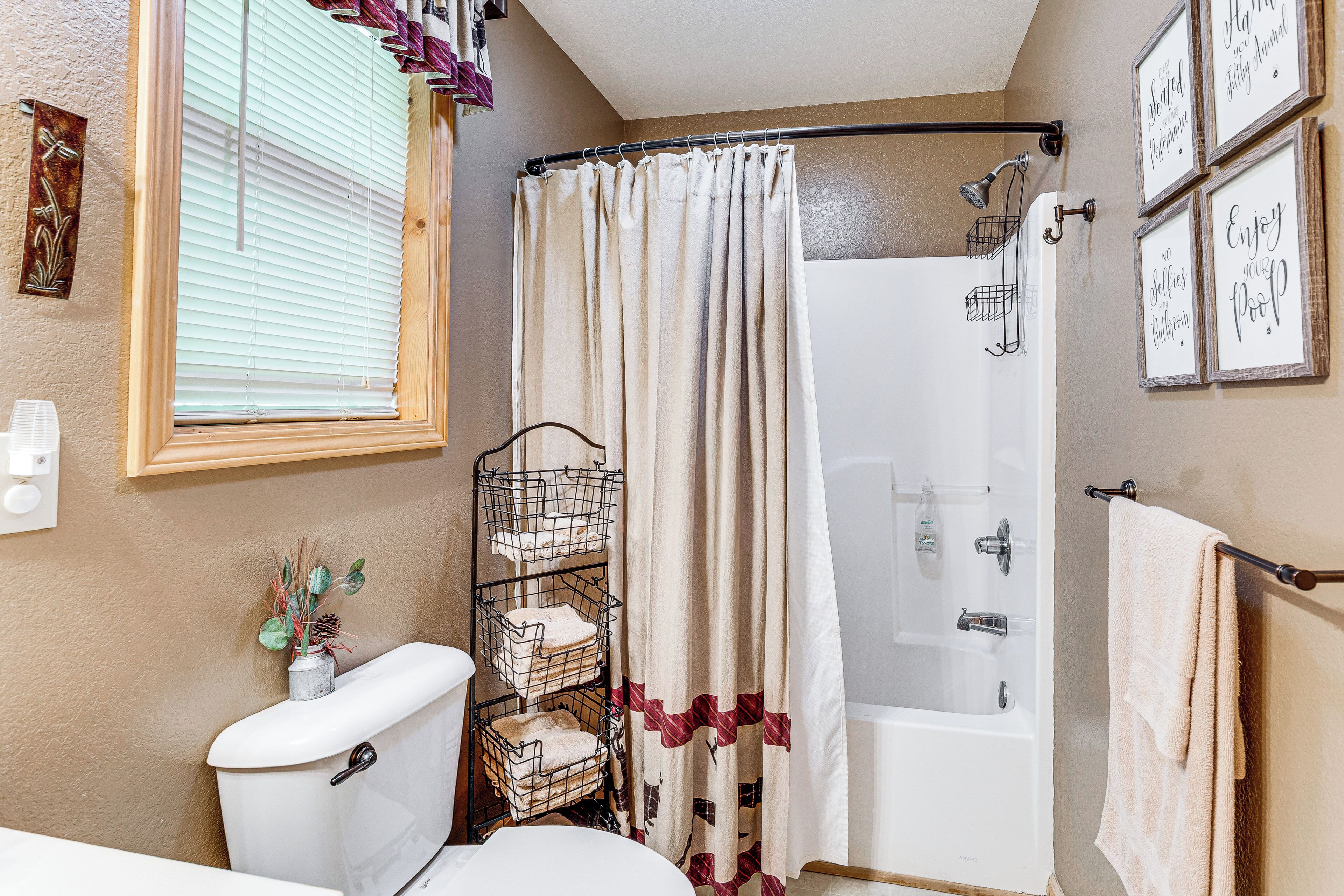 Ein Badezimmer mit Toilette, Dusche und Badewanne. Ein Fenster mit Jalousien, ein Handtuchhalter und ein Regal mit Handtüchern.