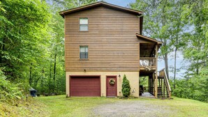 Eine zweistöckige Holzhütte mit Garage, Balkon und Treppe, die zu einer oberen Ebene führt.