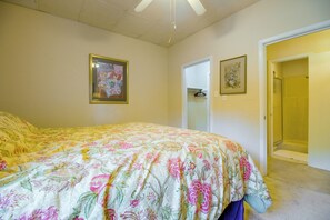 A bedroom with a floral bedspread, a door leading to a bathroom, and a ceiling fan. - Easy Access to UAFS & Downtown! Cozy Apt w/ Patio (Fort Smith)