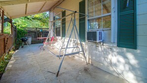 Eine überdachte Terrasse mit einer Metallleiter, einem Grill und einem Fenster mit Klimaanlage.