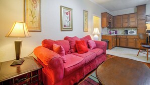 Ein Wohnzimmer mit einem roten Sofa, einem Holztisch und einer Küchenzeile, die aus Holzschränken und einer Mikrowelle besteht.