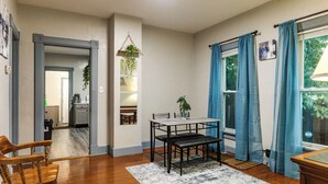 A room with a dining table, chairs, a rug, and a window with curtains.