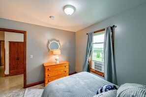 Ein Schlafzimmer mit Bett, Kommode, Spiegel und einem Fenster mit Vorhängen.