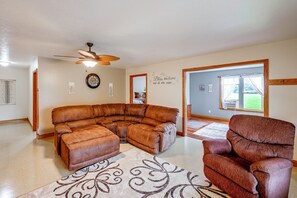 A spacious living room with a large L-shaped sectional sofa, a small armchair, a ceiling fan, and a large window with a view of the outdoors. - Family-Friendly Goshen Home Near Amish Country (Goshen)