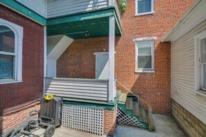 A corner of a building with a brick facade, a white door, and a small porch with a green roof. - Hike, Golf & Explore! Family Gem in Dtwn Bedford (Bedford)