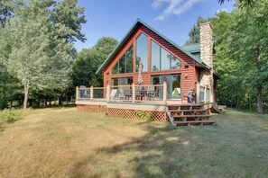 A log cabin with a large deck, surrounded by trees.