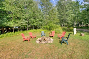 A campsite with a fire pit surrounded by six Adirondack chairs.