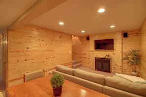 A room with wooden panel walls, a television mounted on the wall, a sofa, a dining table with chairs, and a small potted plant. - Enjoy the Colors of Fall at the Lake House (Brainerd)