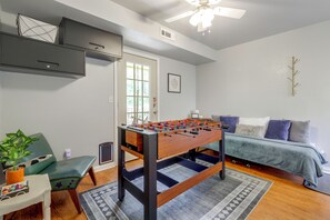 Ein Zimmer mit Tischfußball, einer Couch, einem Sessel, einem kleinen Tisch mit Pflanze und einem Deckenventilator.