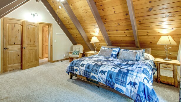 A bedroom with a sloped ceiling, wooden walls, a bed with a blue and white patterned bedspread, two bedside lamps, and a chair. - Minutes to slopes & shore! Cozy cabin w/ hot tub (South Lake Tahoe)