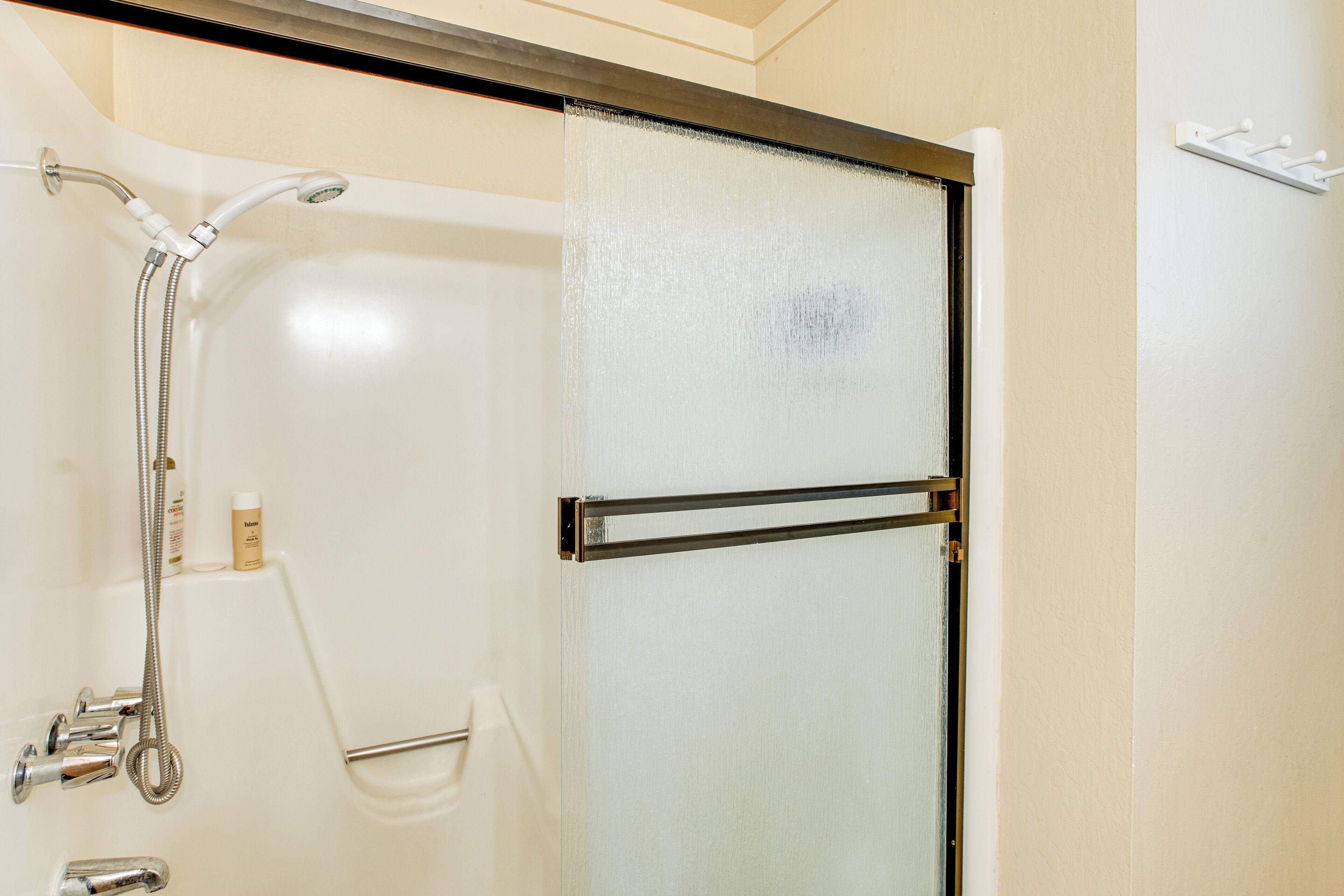 A shower enclosure with a glass door, a handheld showerhead, and a handheld shower attachment.