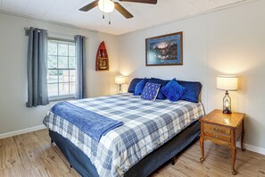 Ein Schlafzimmer mit einem Bett, einem Nachttisch, einer Lampe, einem Fenster mit Vorhängen, einem Deckenventilator und einem Wandregal mit Dekorationen.