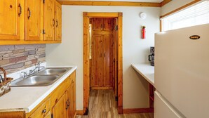 A compact kitchen with wooden cabinets, a double sink, and a refrigerator. - Walk to Park & Creek! Spearfish Couple’s Retreat (Spearfish)