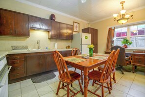 Una cocina con armarios de madera, un refrigerador, una mesa de comedor con sillas y una ventana con cortinas.