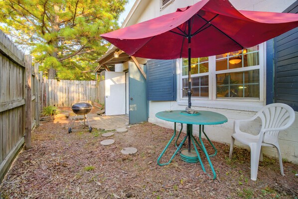 Un patio trasero con una parrilla, una mesa con un paraguas rojo y una silla blanca.