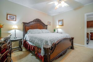 Un dormitorio con una cama de madera grande, dos mesitas de noche con lámparas, un ventilador de techo y vistas a la cocina.