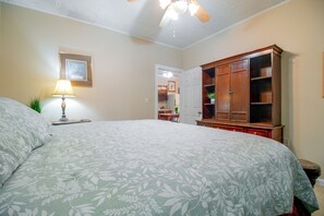 A bedroom with a large bed, a wooden wardrobe, a desk with a chair, and a lamp.