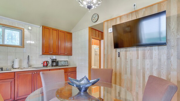 A modern kitchen with wooden cabinets, a glass dining table, and a flat-screen TV mounted on the wall. - 2-Unit Combo, 6 Mi to Bethel Woods Center! (Mongaup Valley)