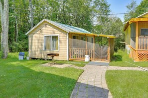 Eine kleine Holzhütte mit Veranda, umgeben von einem grünen Rasen und Bäumen.