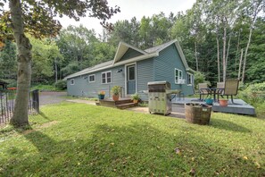 A small, single-story house with a front porch, surrounded by a grassy yard and trees. - Deck & Stunning Views! Family Getaway in Hamilton (Hamilton)