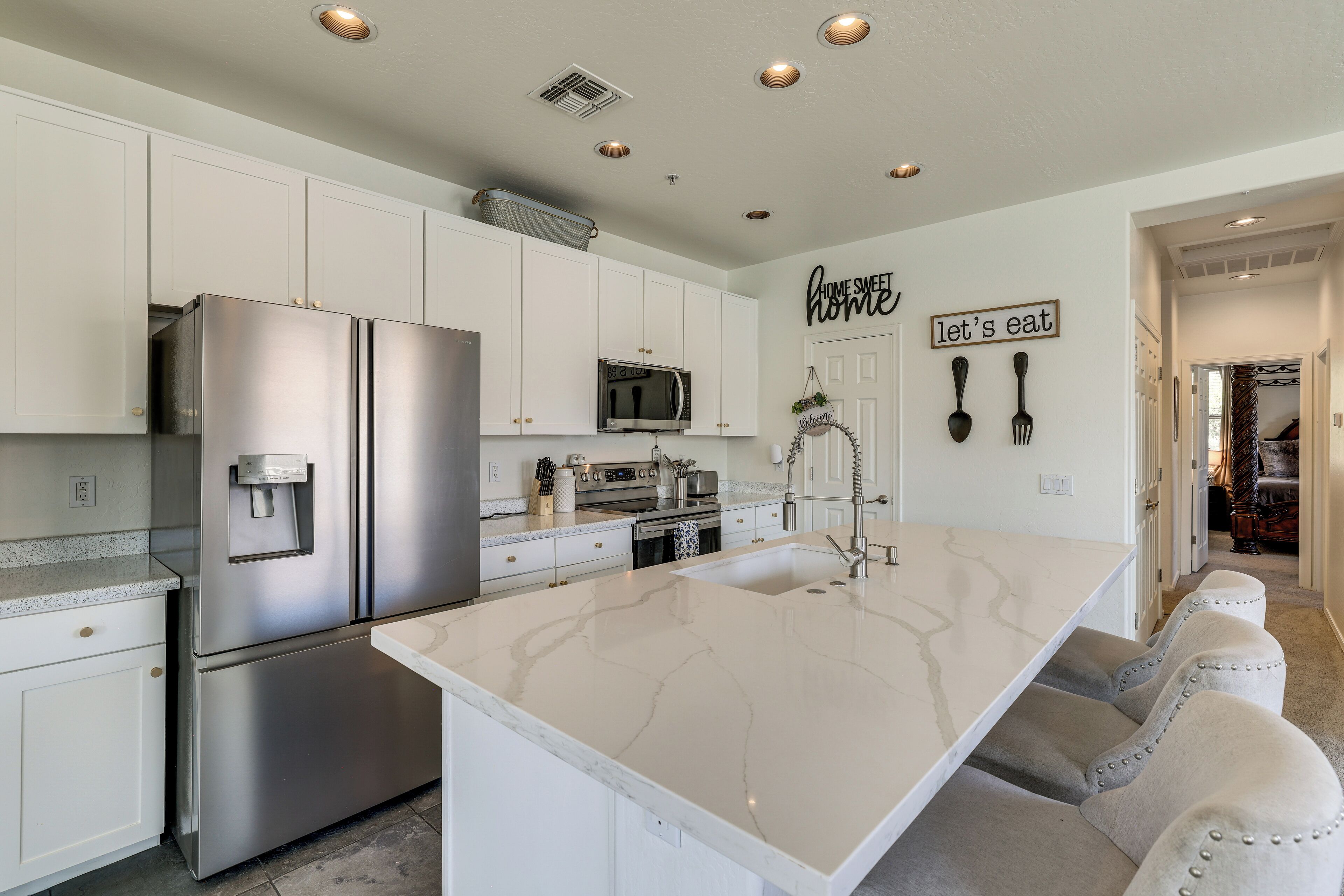A modern kitchen with white cabinetry, stainless steel appliances, and a marble island.