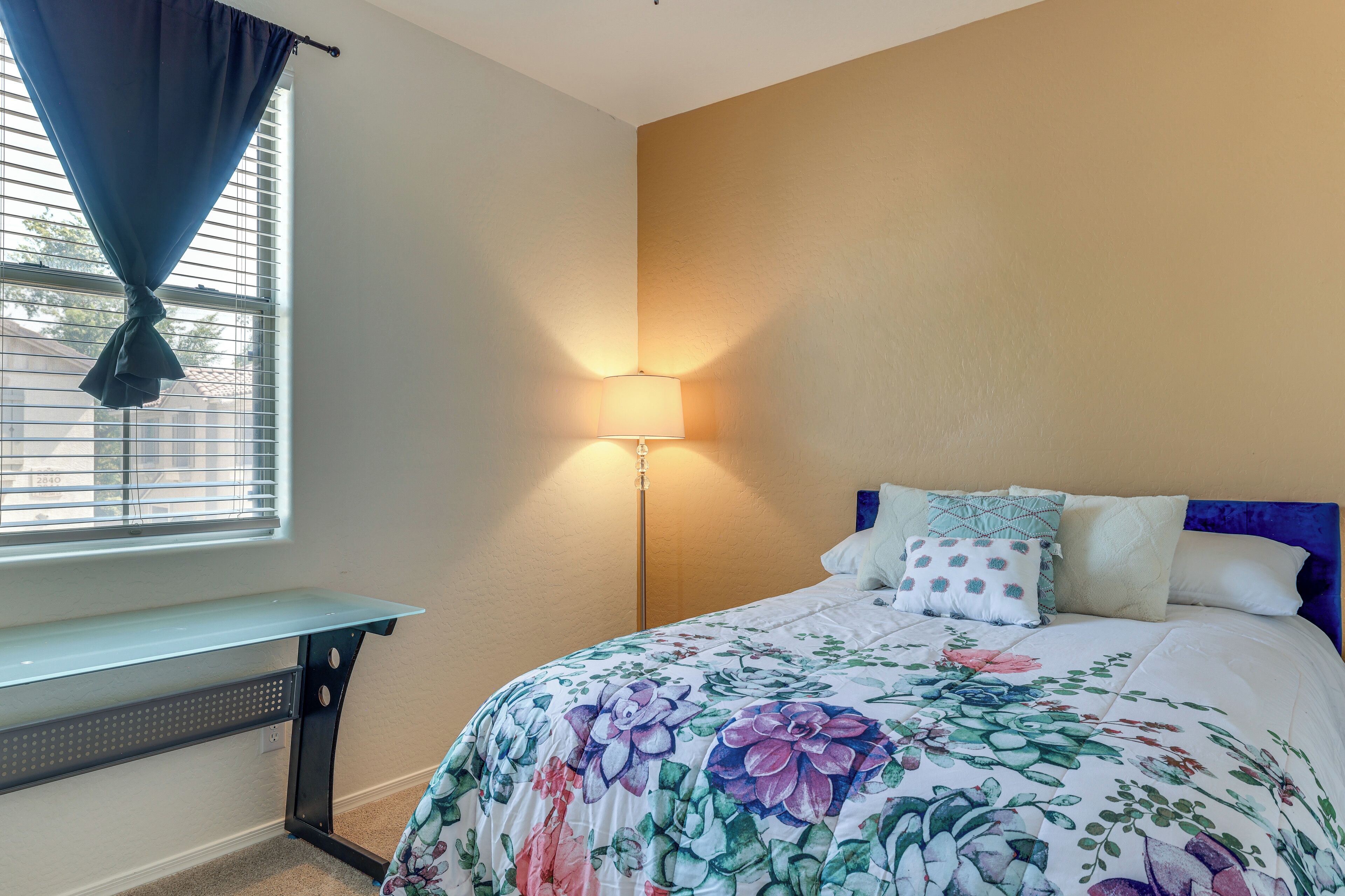 Um quarto com uma cama, uma mesa de cabeceira, uma luminária e uma janela com cortinas.