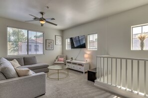A living room with a grey sofa, a small round table, a white cabinet, a television mounted on the wall, and a ceiling fan. - Relax Poolside, Explore South Mtn! Extended Escape (Phoenix)
