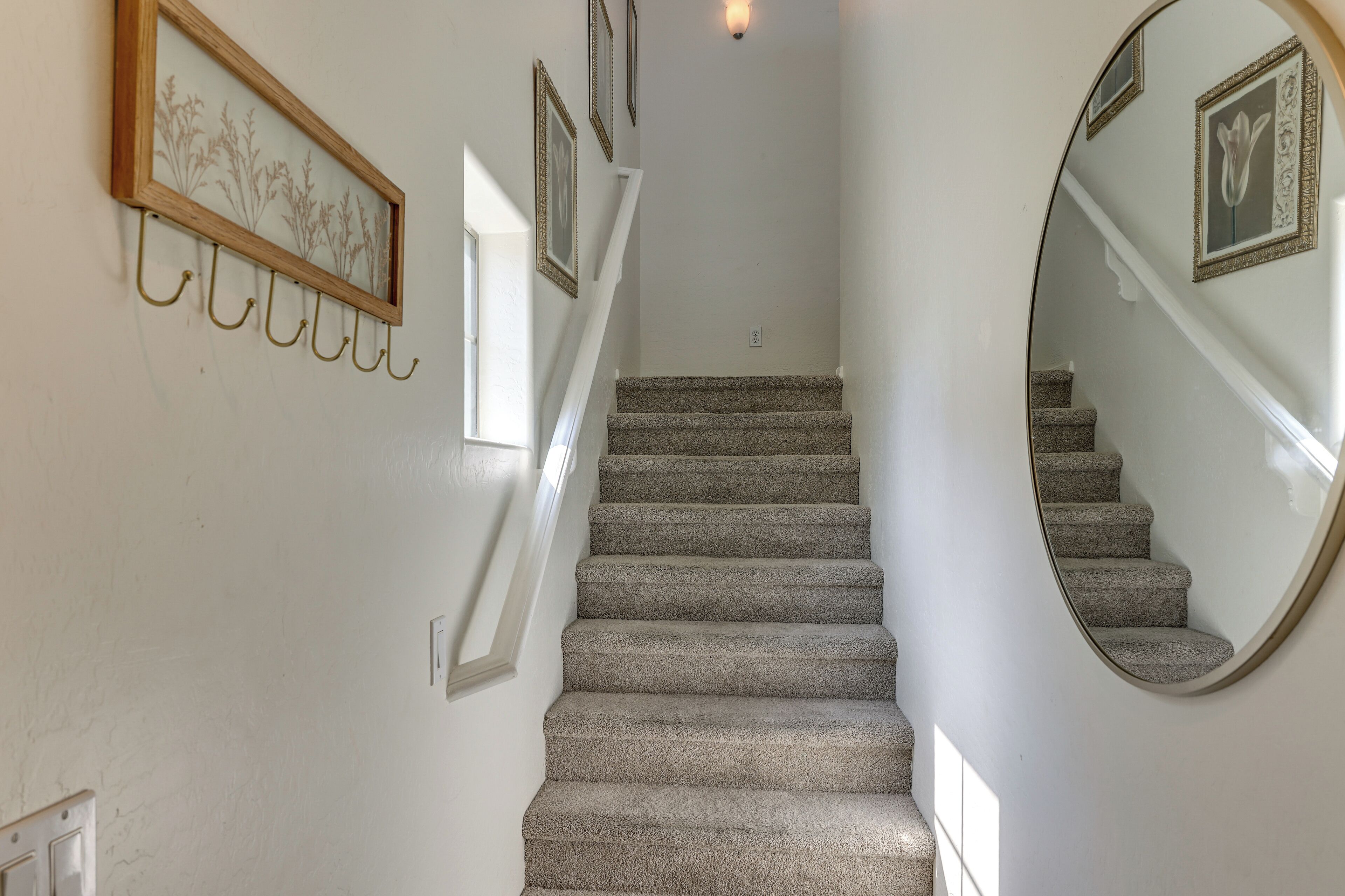 A staircase with carpeted steps, a wall-mounted mirror, and several framed pictures.