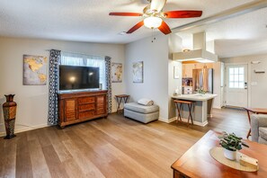 A spacious living room with hardwood flooring, a large flat-screen TV, a wooden entertainment center, and a ceiling fan.