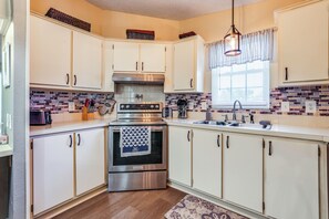 A kitchen with white cabinets, a stainless steel oven, a microwave, and a window with curtains.