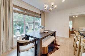 A dining area with a wooden table, cushioned chairs, a fur rug, and a view of the outdoors through large windows. - Walkable Rose District Retreat! 15 Mi to Tulsa (Broken Arrow)