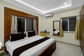 Ein Hotelzimmer mit einem großen Bett, einem Schreibtisch, einer Klimaanlage, einem Spiegel und einem Kleiderschrank.