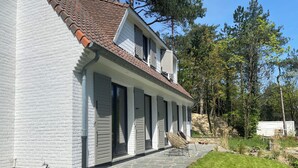 Et toetagers hus med hvide facader, et tagtækket tag og en overdækket veranda med stole.