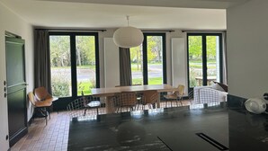 Et moderne spiseområde med et stort bord og stole, store vinduer med gardiner samt en hængende lampe.
