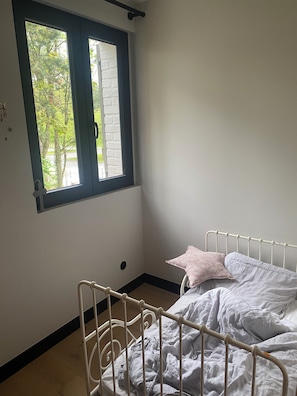 A room with a single bed, a window with a view of trees, and a white wall.