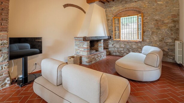 A cozy room with a stone fireplace, a flat-screen TV, and two cushioned seating areas. - Casale le Lupe Apartments - Ground Floor (Campiglia Marittima)