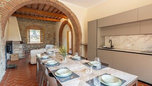A dining area with a long table set for six, a kitchen with marble backsplash, and a stone fireplace. - Casale le Lupe Apartments - Ground Floor (Campiglia Marittima)