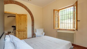 A bedroom with a bed, a chair, a wooden door, and a window. - Casale le Lupe Apartments - Ground Floor (Campiglia Marittima)