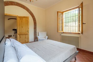 Un dormitorio con una cama, una silla, una puerta de madera y un ventanal.