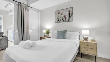 A modern bedroom with a large bed, a nightstand with a lamp, a potted plant, and a painting on the wall.