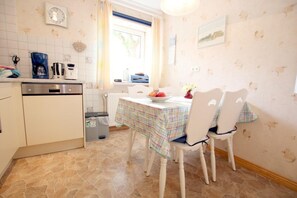 A kitchen with a dining table, chairs, and a clock on the wall. - Babendörpstieg 20, Apt. 2 - Nieblum - 3-room vacation apartment in Nieblum, approx. 75 square meters (Nieblum)