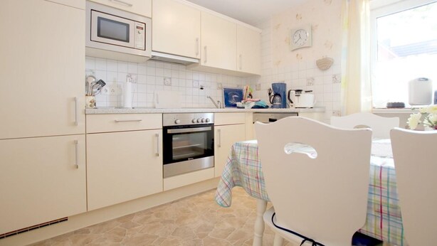A kitchen with white cabinets, a microwave, an oven, and a dining area with a table and chairs. - Babendörpstieg 20, Apt. 2 - 3-room vacation apartment in Nieblum, approx. 75 square meters, on the ground floor, with (Nieblum)
