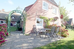 A patio with a table and chairs, a brick house, and a green archway. - Babendörpstieg 20, Apt. 2 - Nieblum - 3-room vacation apartment in Nieblum, approx. 75 square meters (Nieblum)