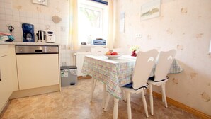 A kitchen with a dining table, chairs, and a clock on the wall. - Babendörpstieg 20, Apt. 2 - 3-room vacation apartment in Nieblum, approx. 75 square meters, on the ground floor, with (Nieblum)