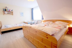 A bedroom with two wooden beds, a white chair, a small shelf with books and a bird figurine, and a window with curtains. - Babendörpstieg 20, Apt. 1 - Nieblum - 2-room vacation apartment in Nieblum, approx. 55 square meters (Nieblum)